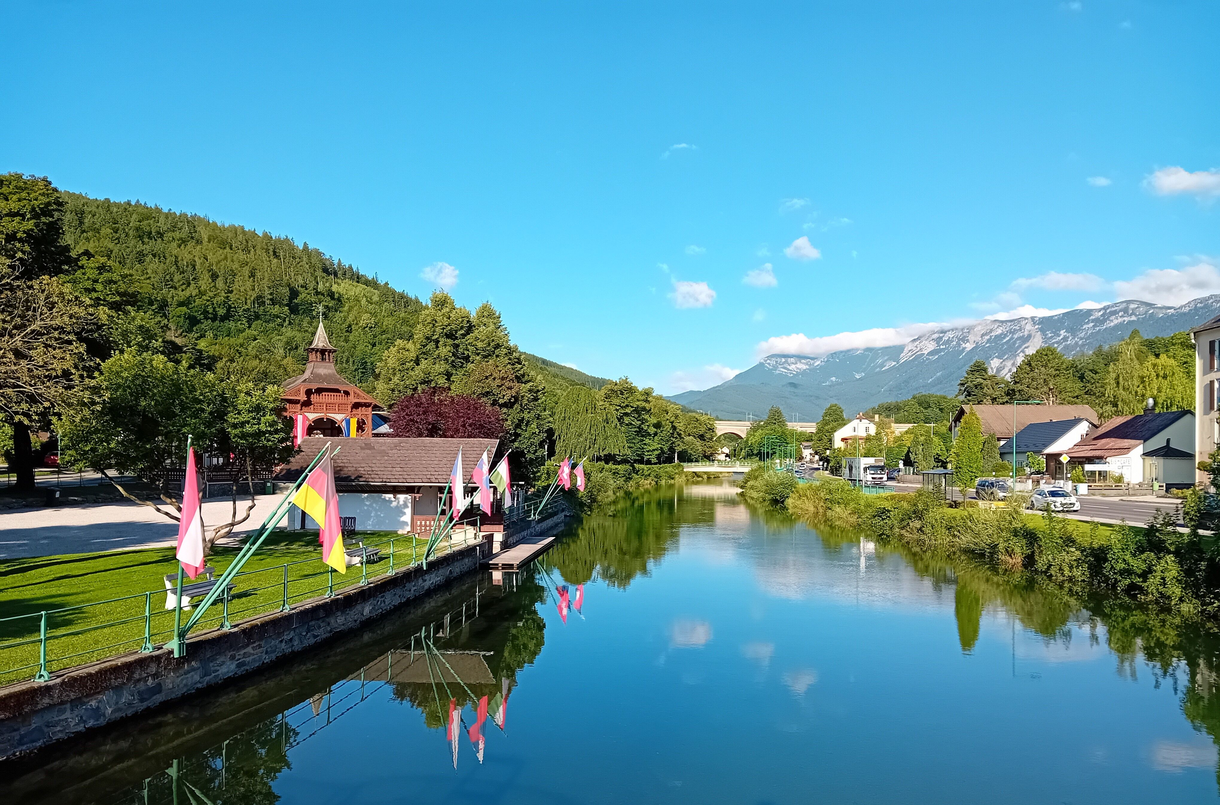 River landscape in Payerbach with mountains in the background and flags along the banks.