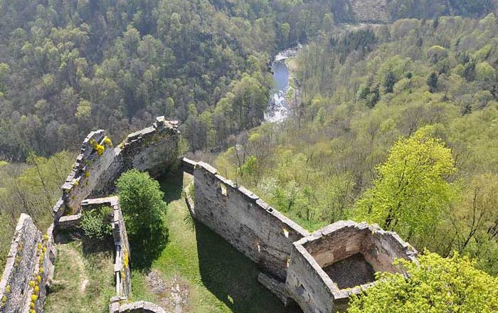 Ruins of an old castle with a view of wooded hills and a river in the background.