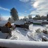 Winter glamping park with snow-covered huts and trees under blue skies and sunshine.