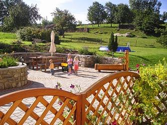 Garden with terrace, playground and green meadow in the background.