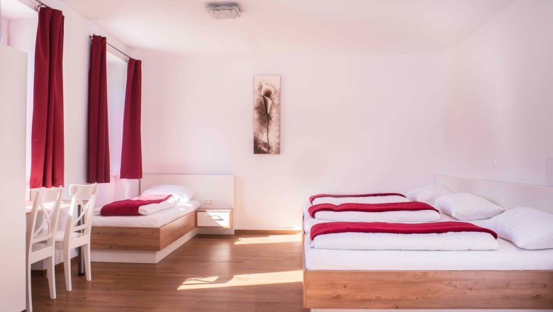 Bright room with two beds, red curtains and a picture on the wall.