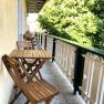 Wooden balcony with table and chairs, green trees next to it.