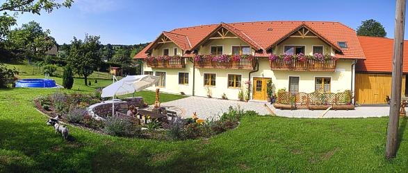 A large yellow house with red roofs and flower boxes, surrounded by a well-tended garden with a seating area and parasol.