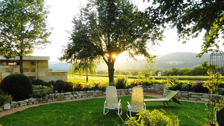 A garden with sun loungers, trees and a stone wall at sunset.
