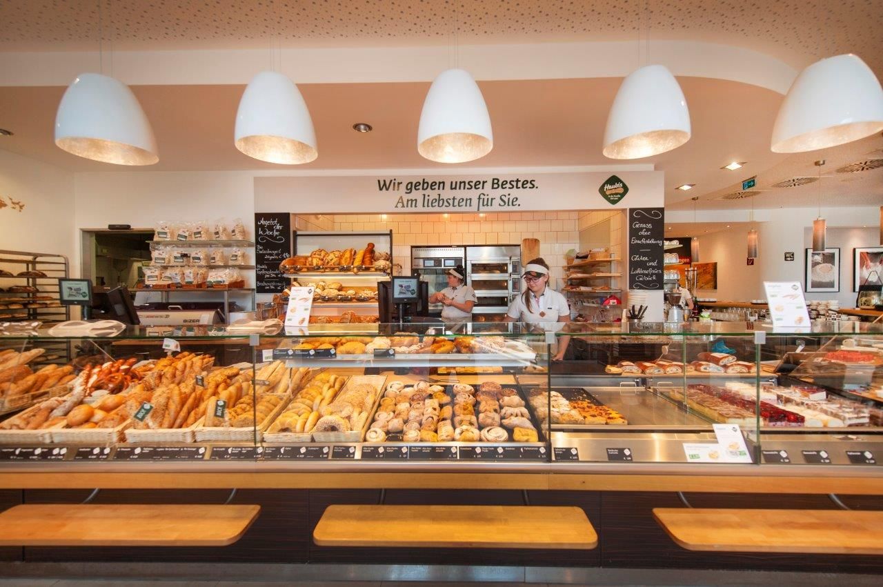 Interior view of a bakery with a counter full of baked goods and two employees.