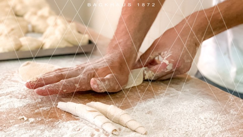 Person shaping dough on a floured table in a bakery.