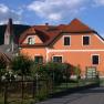 An orange-colored house with red roof tiles and a church tower in the background.