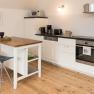 Modern kitchen with white furnishings, wooden floor and small dining table with two stools.