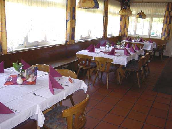 A dining room with laid tables, white tablecloths and purple napkins. Wooden chairs and large windows are visible.
