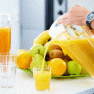 Person pours orange juice from a jug into a glass, surrounded by fresh fruit.