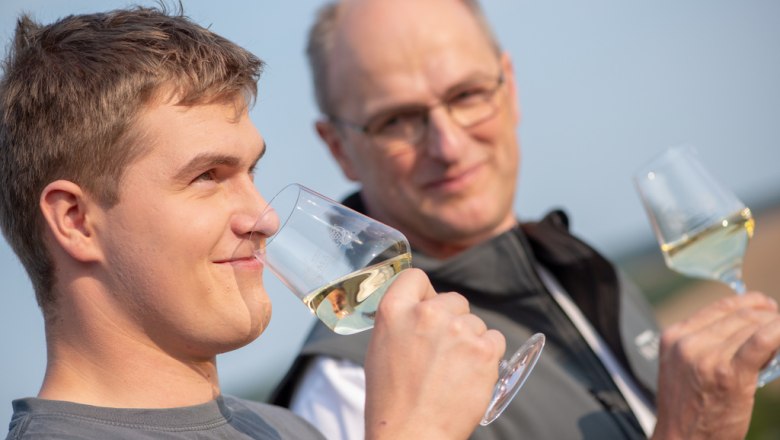 Two men enjoy white wine outdoors.