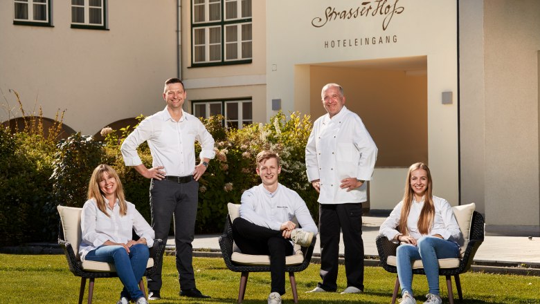 Five people pose in front of a building with the inscription 'Eisenbock's Strasserhof Hotel Entrance'.