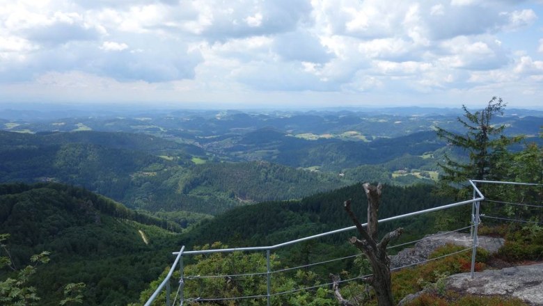 View from the castle stone wall over wooded hills and valleys under a cloudy sky.