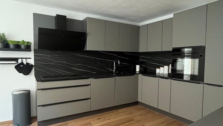 Modern gray kitchen unit with black worktops and wooden floor.