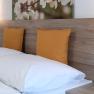 Double bed with wooden back panel, yellow cushions and wall lamps.