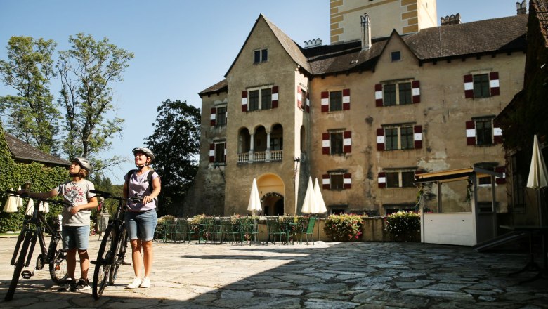 Two people with bicycles are standing in front of Ottenstein Castle.