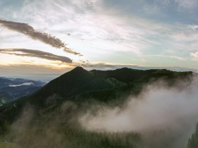 Panoramic view of the Sonnwendstein at sunrise with fog and a lookout tower in the foreground.
