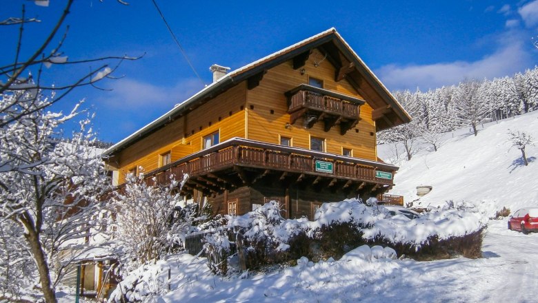 A wooden house in the snow with a blue sky in the background.