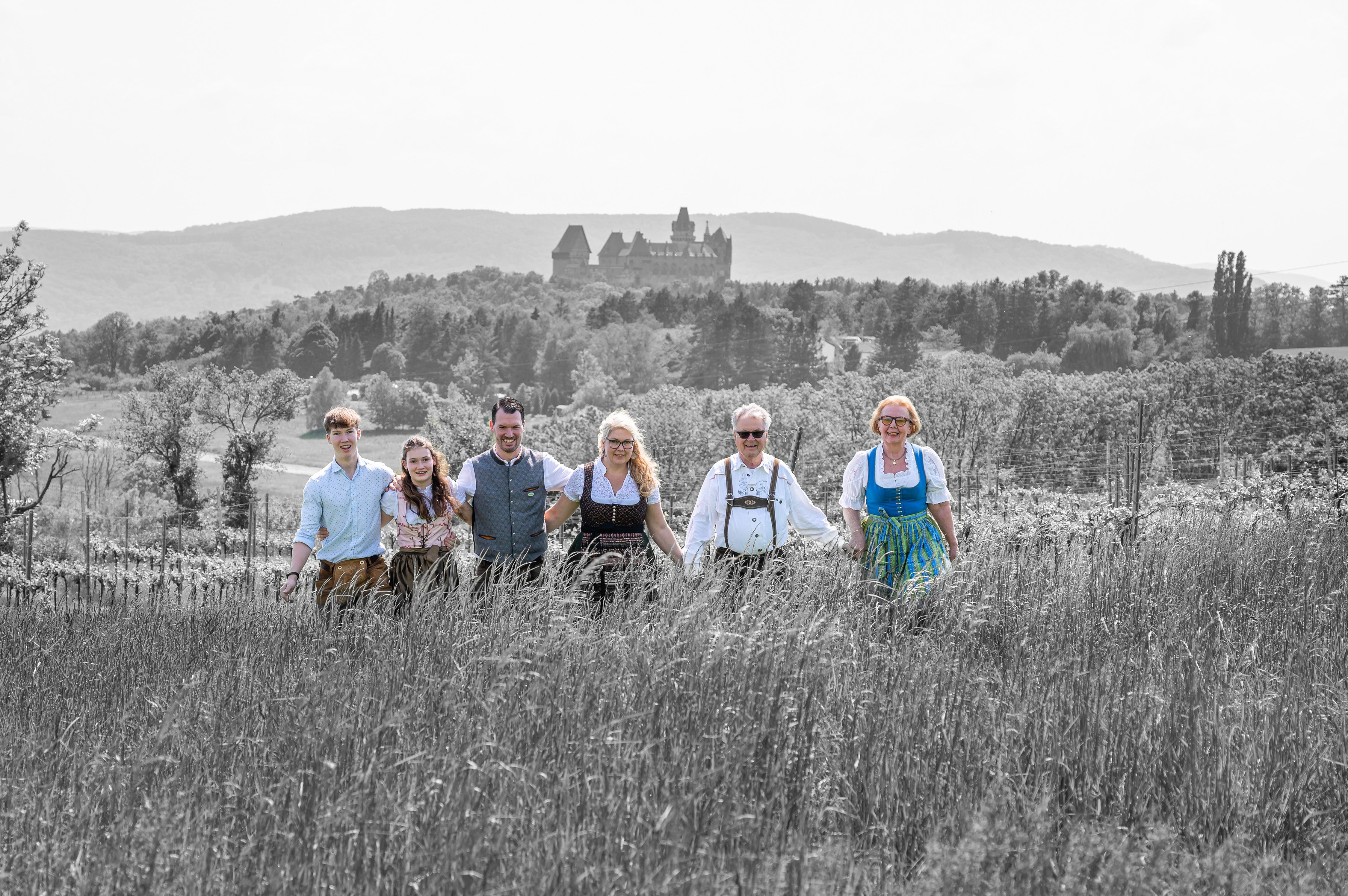 A group of six people in traditional dress stand in a field with a castle in the background.