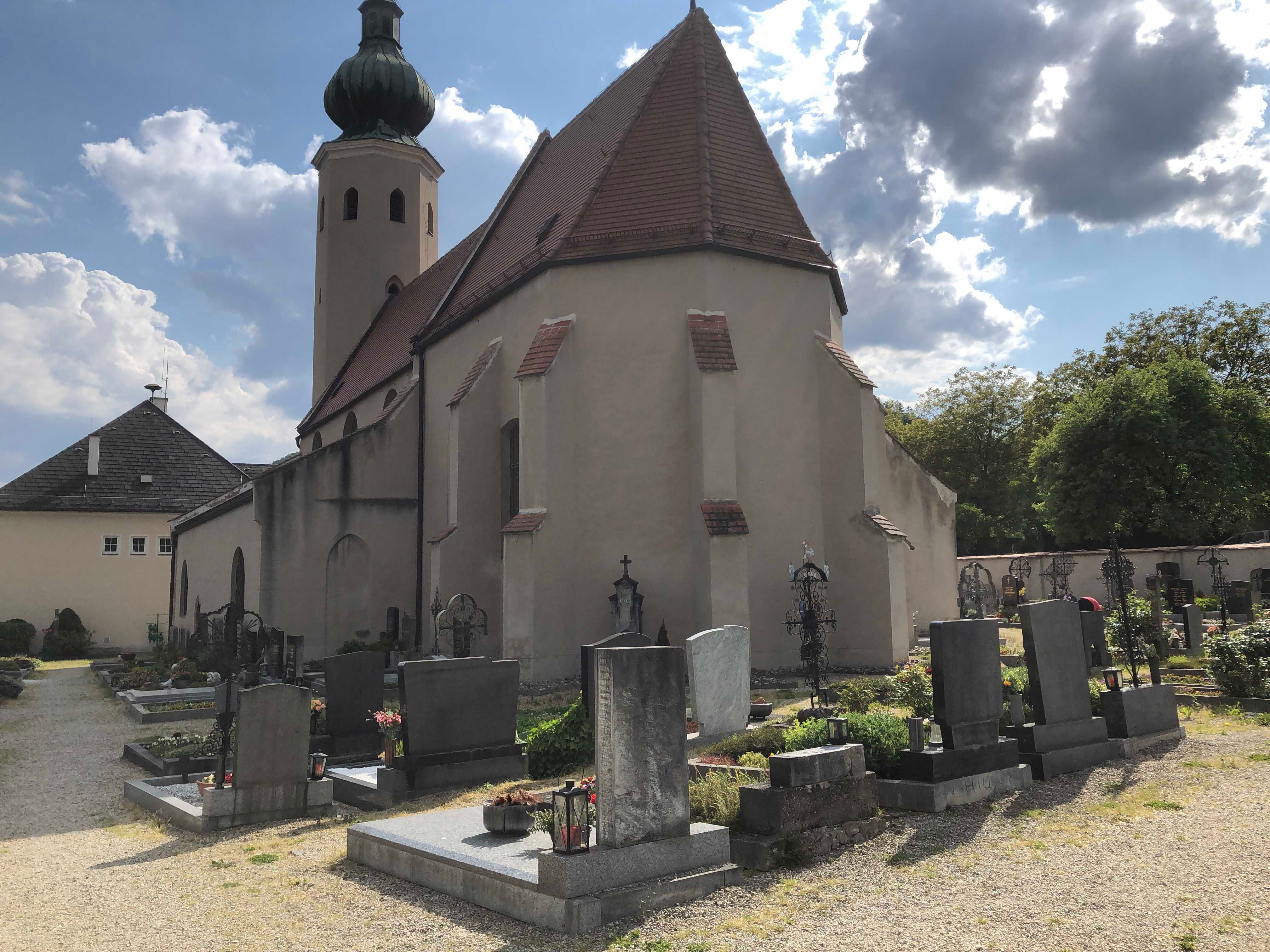 Church with cemetery and gravestones in the foreground, cloudy sky.