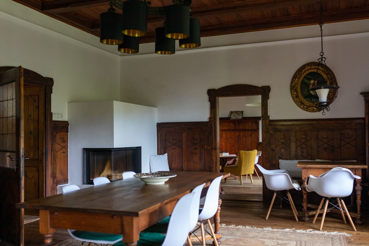 Dining room with wooden table, white chairs and fireplace.