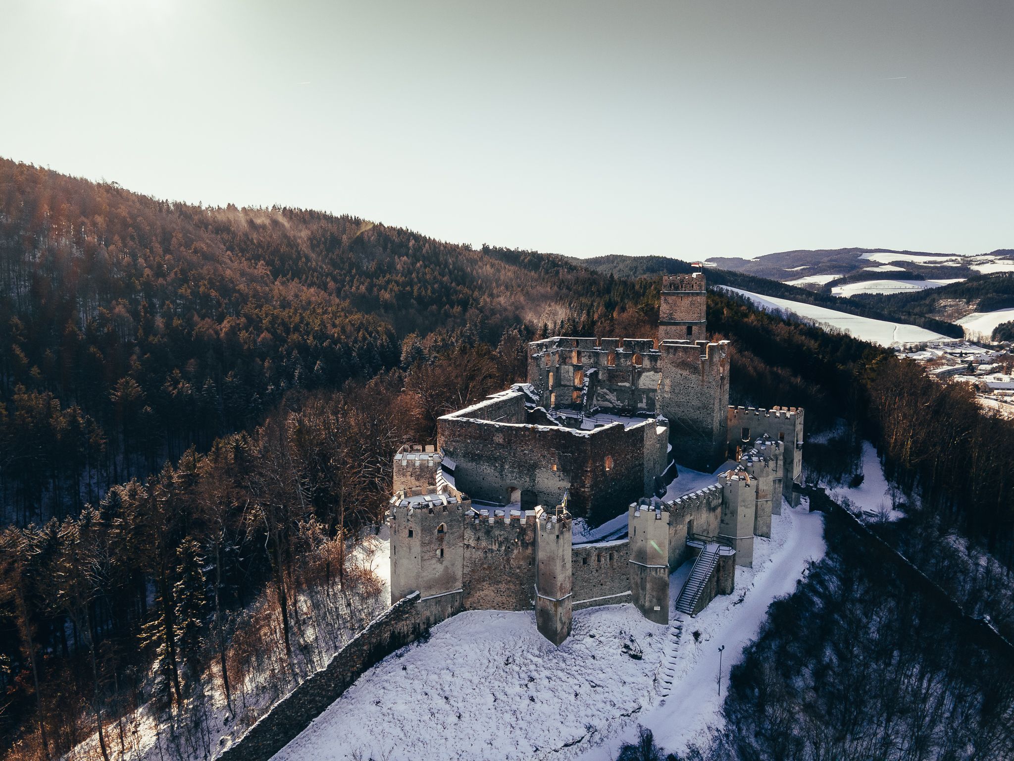 Aerial view of the ruins of Kirchschlag Castle in winter, surrounded by snow-covered forests.