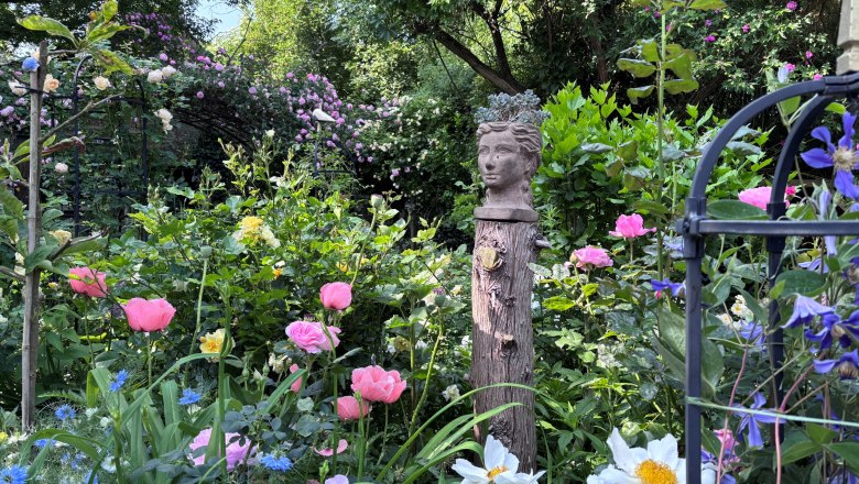A blooming garden with colorful flowers and a bust on a wooden post.