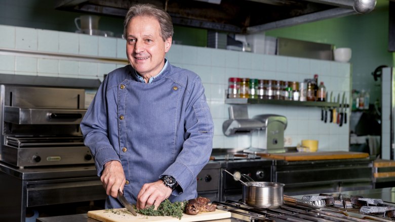 A cook in a kitchen cuts herbs on a chopping board.