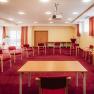 A seminar room with a red carpet, circle of chairs, table, flipchart and projector.