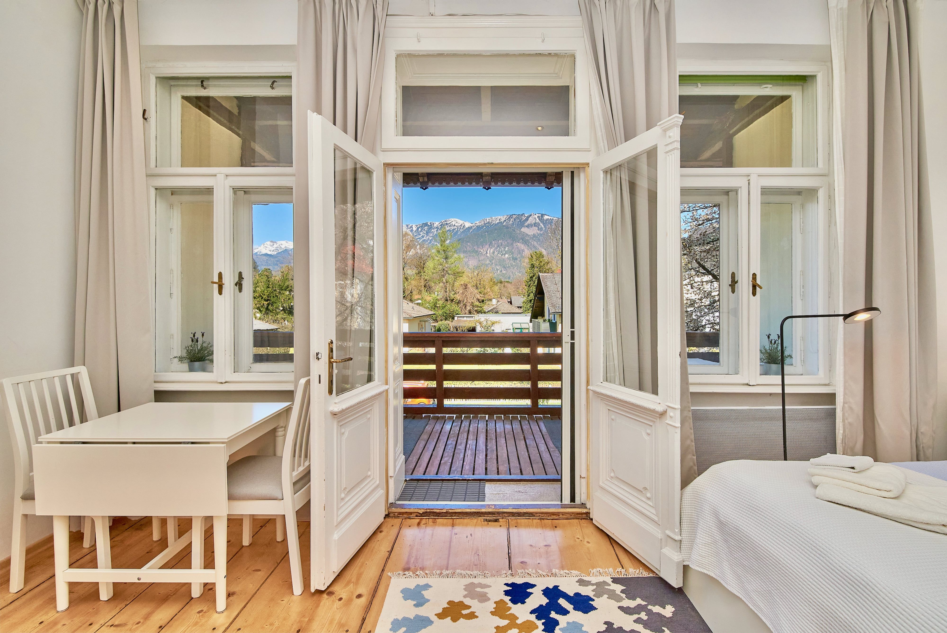 Interior with wooden floor, table, chairs and view of the balcony and mountains.