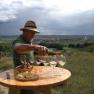 Man pouring wine into glasses on an outdoor table with a view of vineyards and village in the background.
