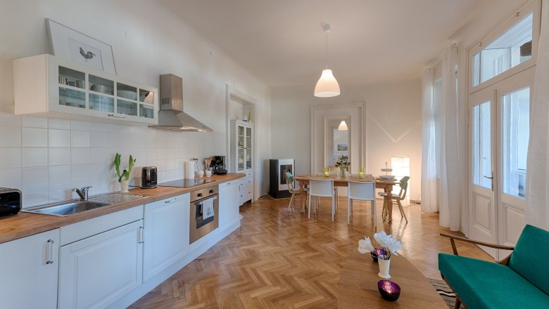 Modern kitchen with dining table, white cupboards and wooden floor.
