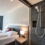 Modern hotel room with double bed and open shower.