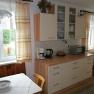 Cozy kitchen with wooden furniture, table, chairs, coffee machine and microwave. Window with curtains, view of the garden.