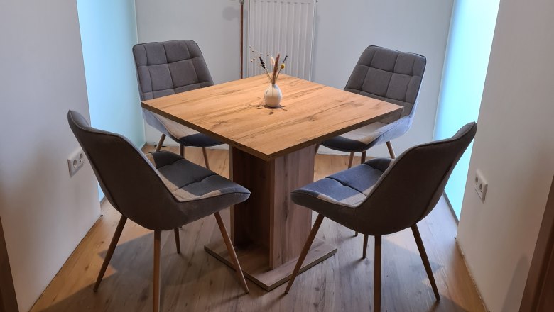 A modern dining table with four gray chairs in a bright room.