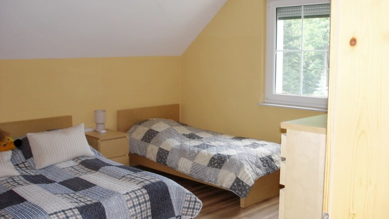 Two single beds in a yellow-painted bedroom with sloping ceiling and window.