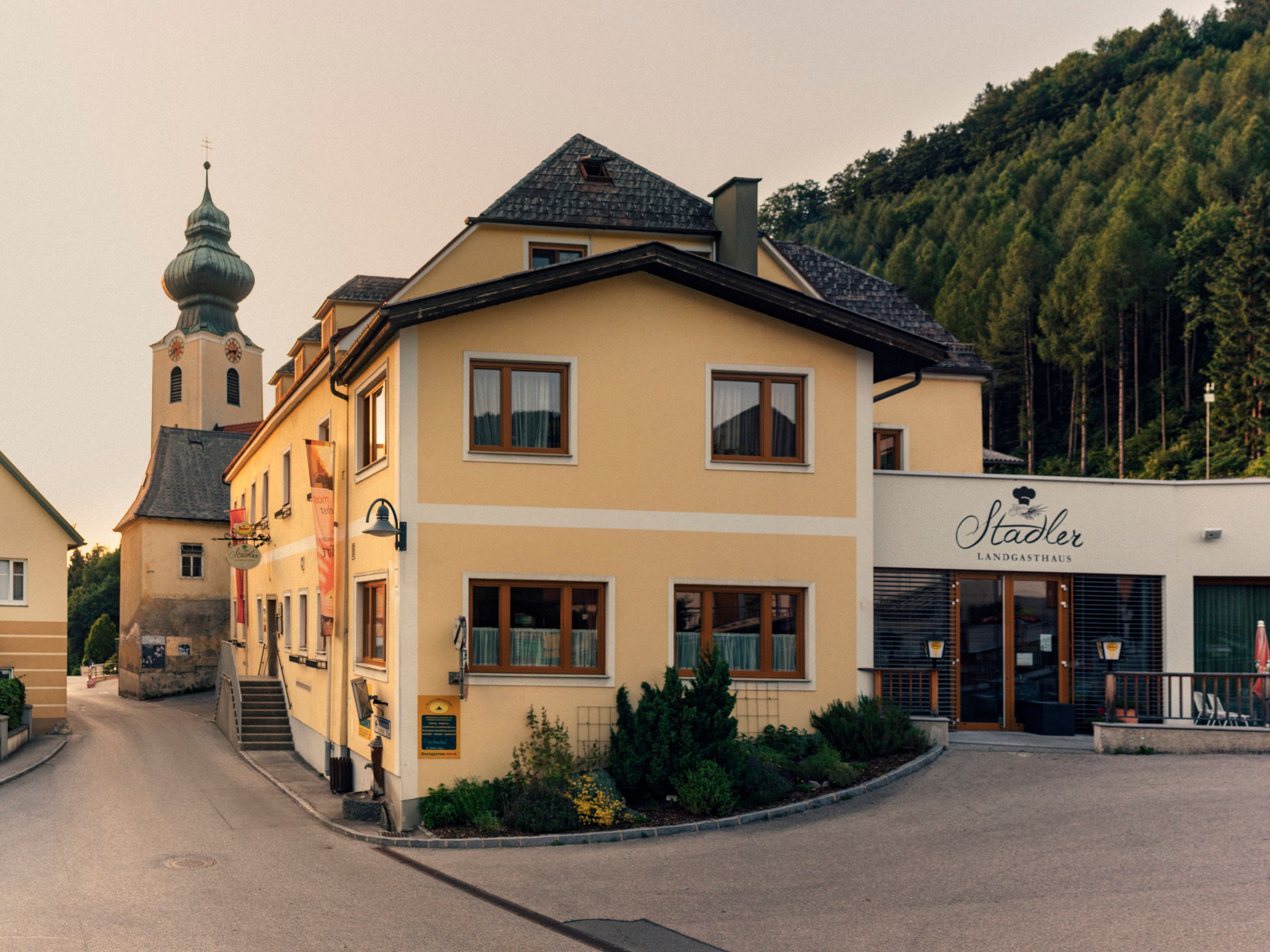 Yellow building with the inscription 'Stadler Landgasthaus' and a church in the background.