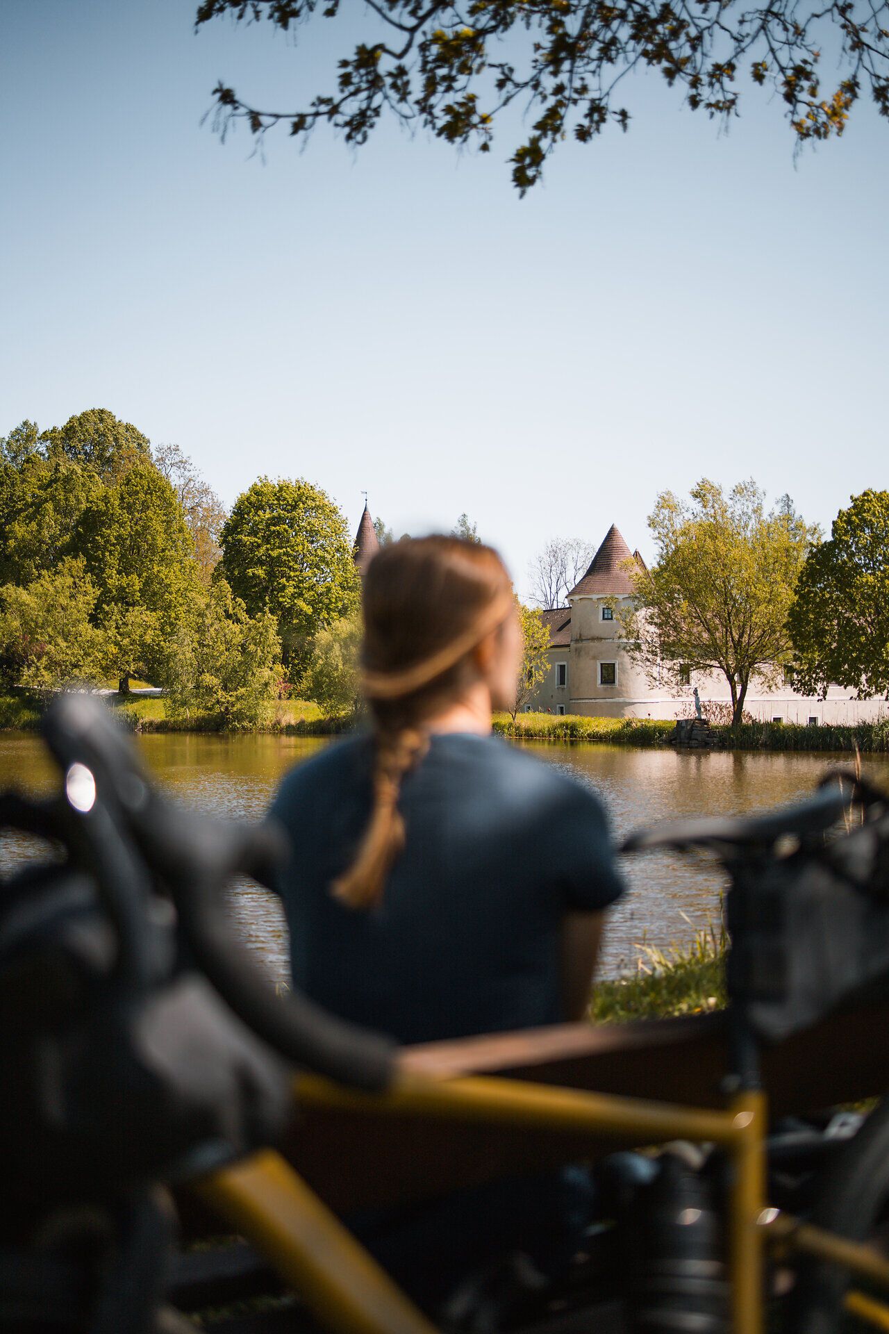 A gentle breeze blows over the glistening water, while the trees glow in lush green. The picturesque backdrop of the castle invites cyclists to take a well-earned break and enjoy the beauty of nature.