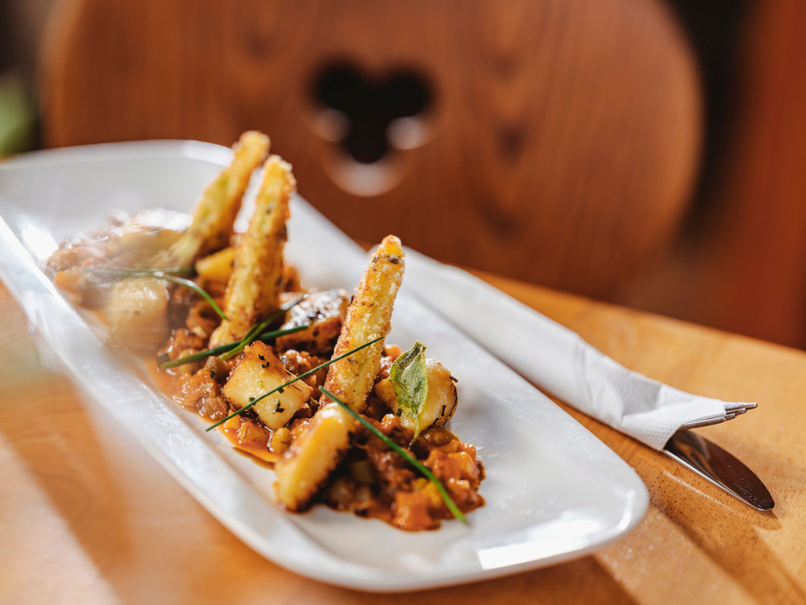 Gourmet dish on a white plate with deep-fried vegetable sticks and herbs.
