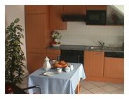 Small kitchen with wooden furniture, dining table with blue tablecloth and crockery.