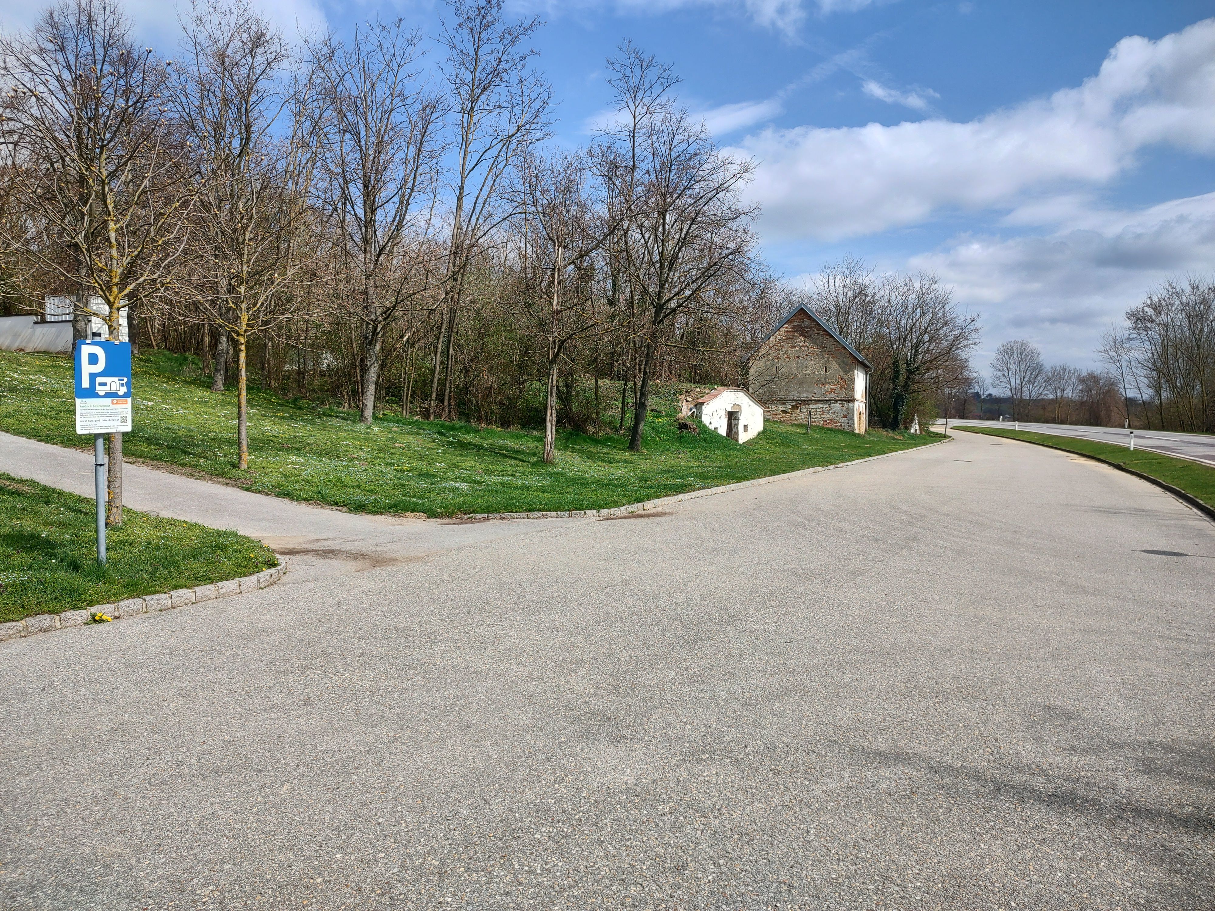 Parking lot with motorhome parking sign, trees and old building in the background.