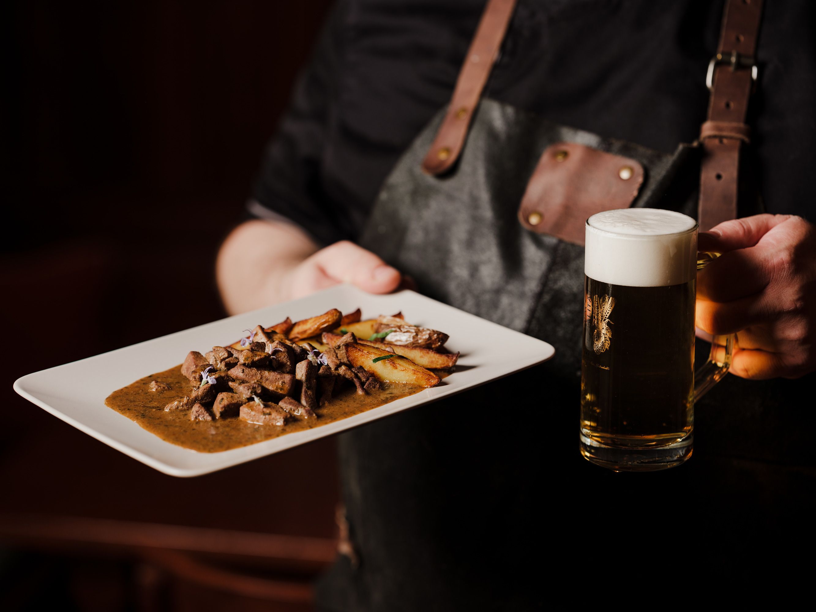 Person holding plate with meat dish and beer mug.