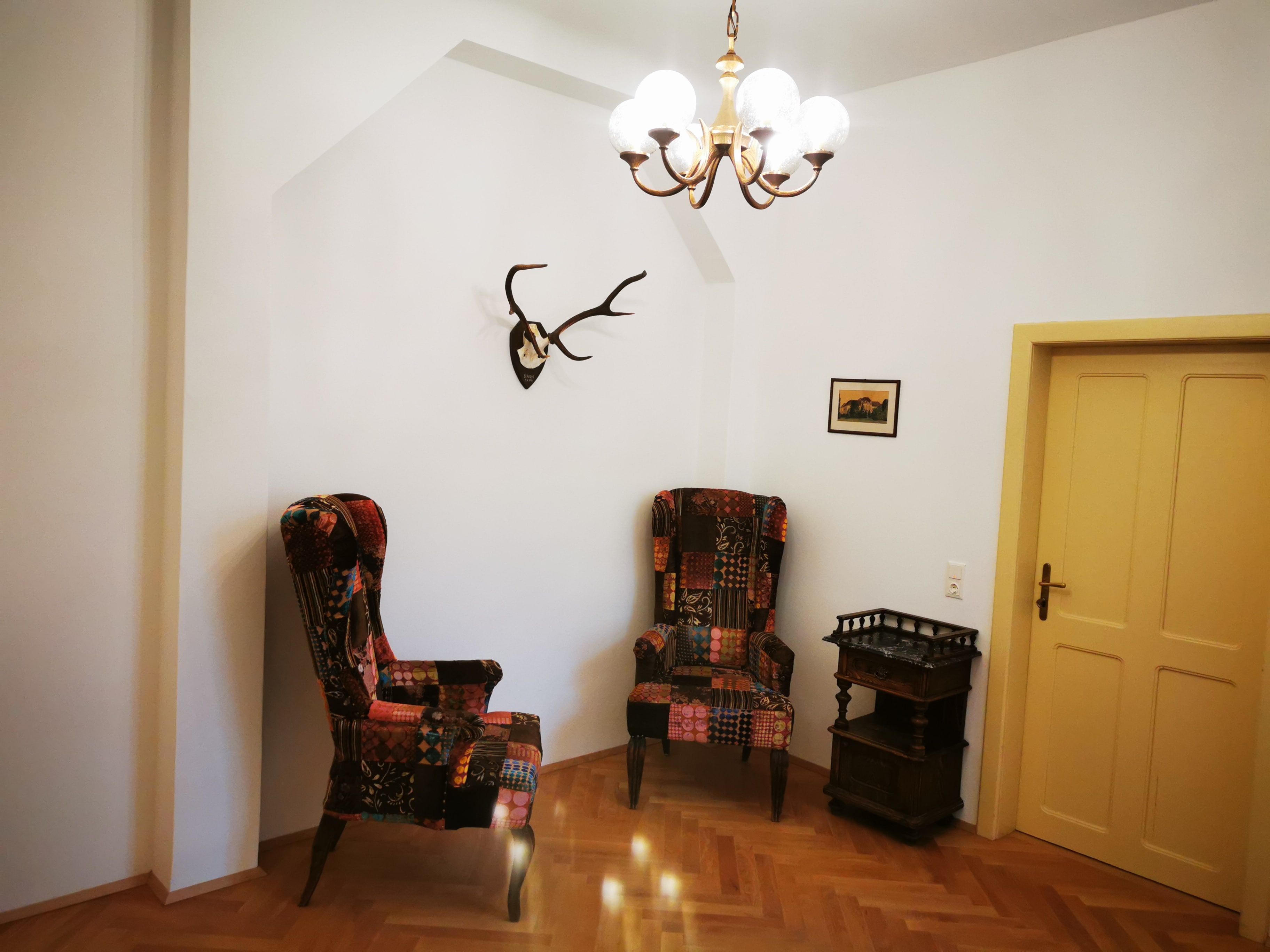 Anteroom with two colorful armchairs, antlers on the wall, small table and yellow door.