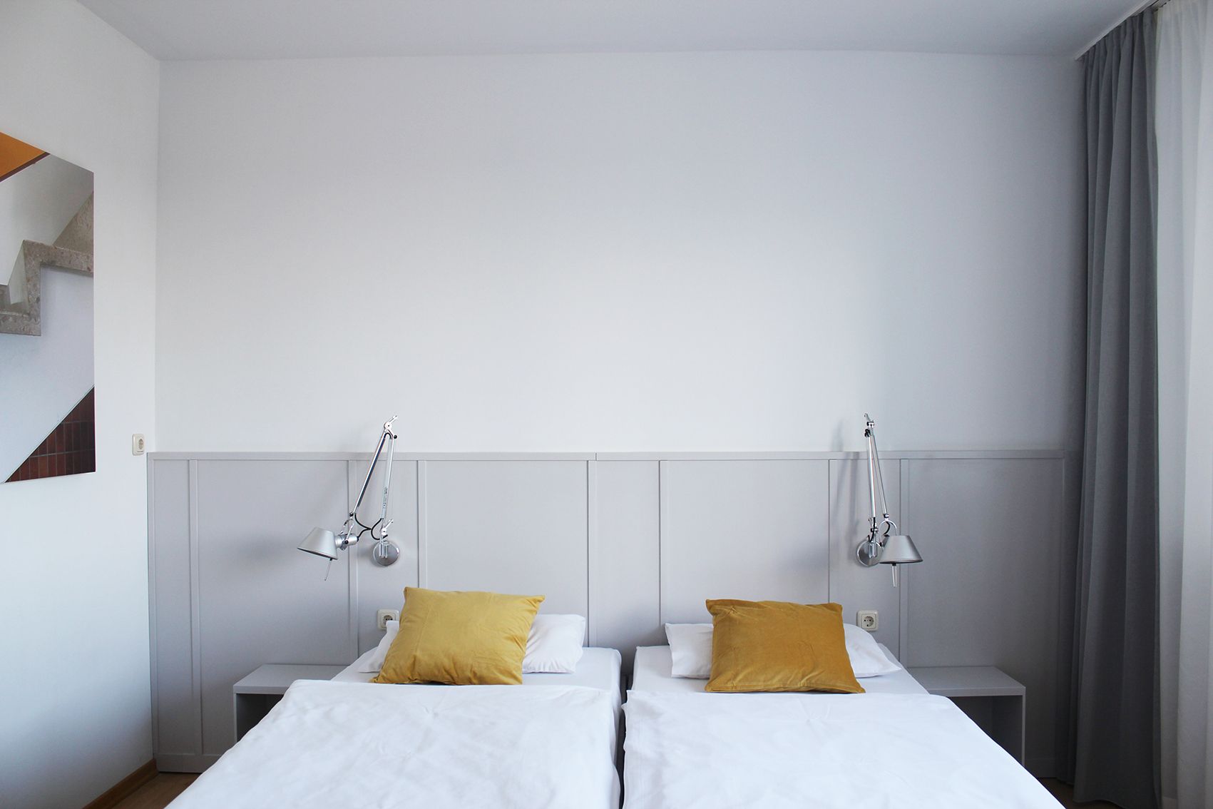 Modern guest room with two single beds, yellow cushions and wall lamps.