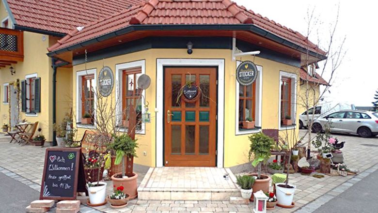 Entrance to the Stocker farm store with yellow façade, red roof tiles and plants and decorations in the foreground.