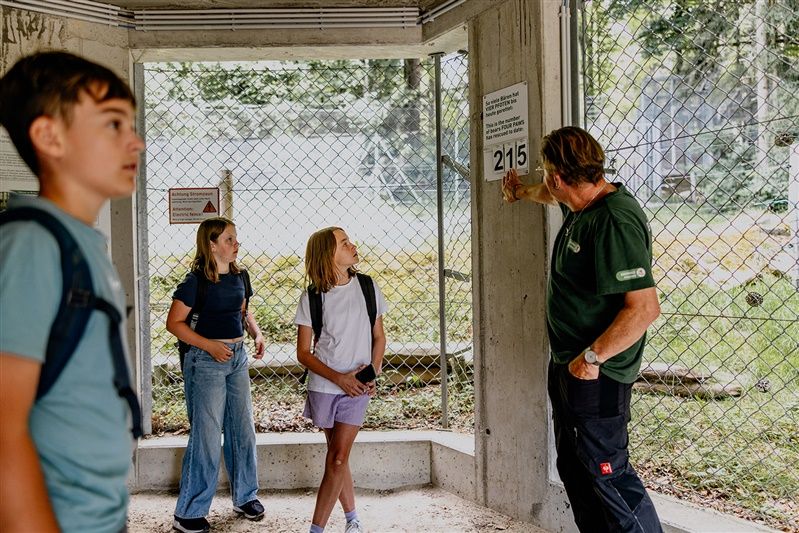 A man shows three children a sign in an enclosure in the Arbesbach bear sanctuary.
