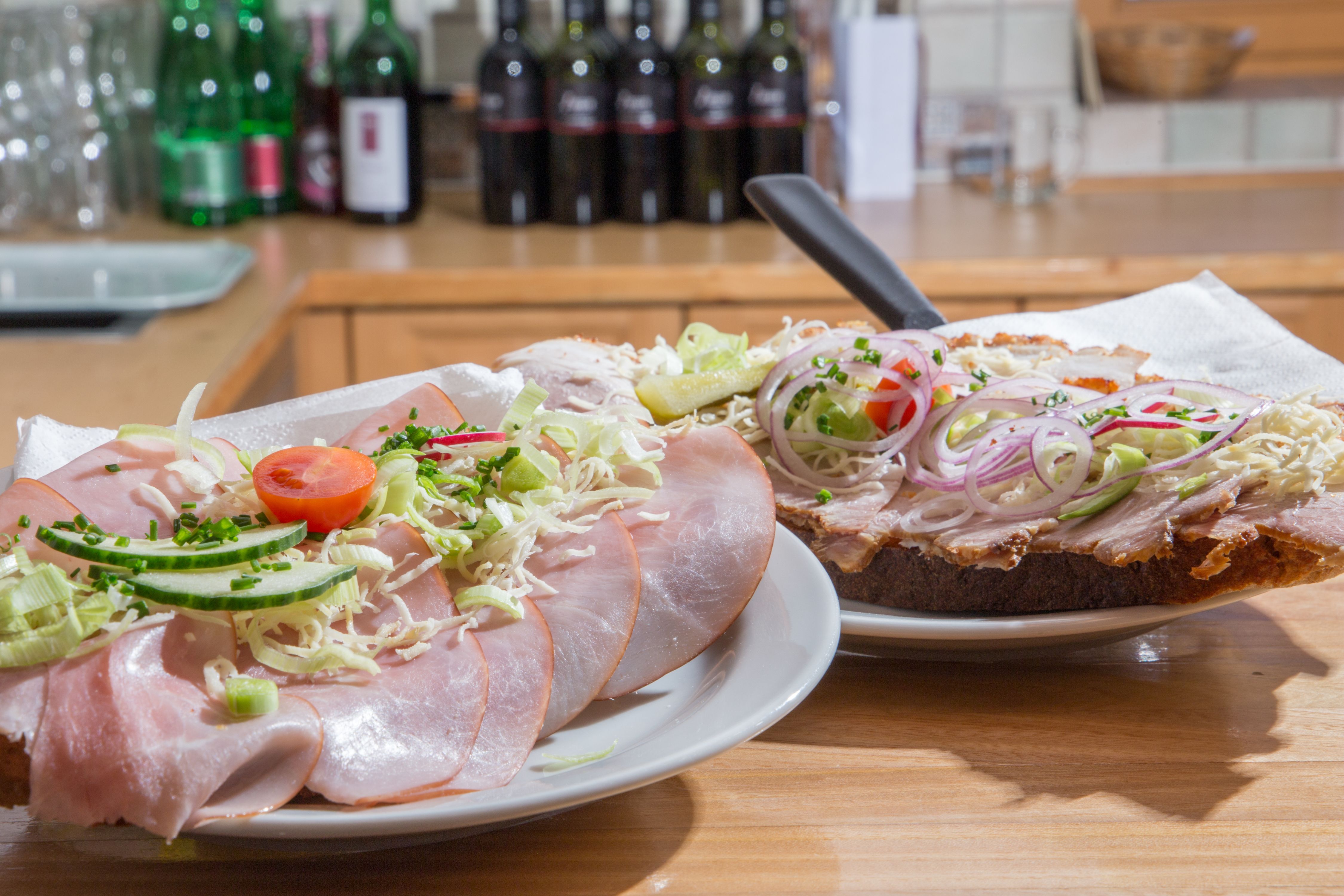 Two sandwiches with ham, onions and vegetables on a wooden table.