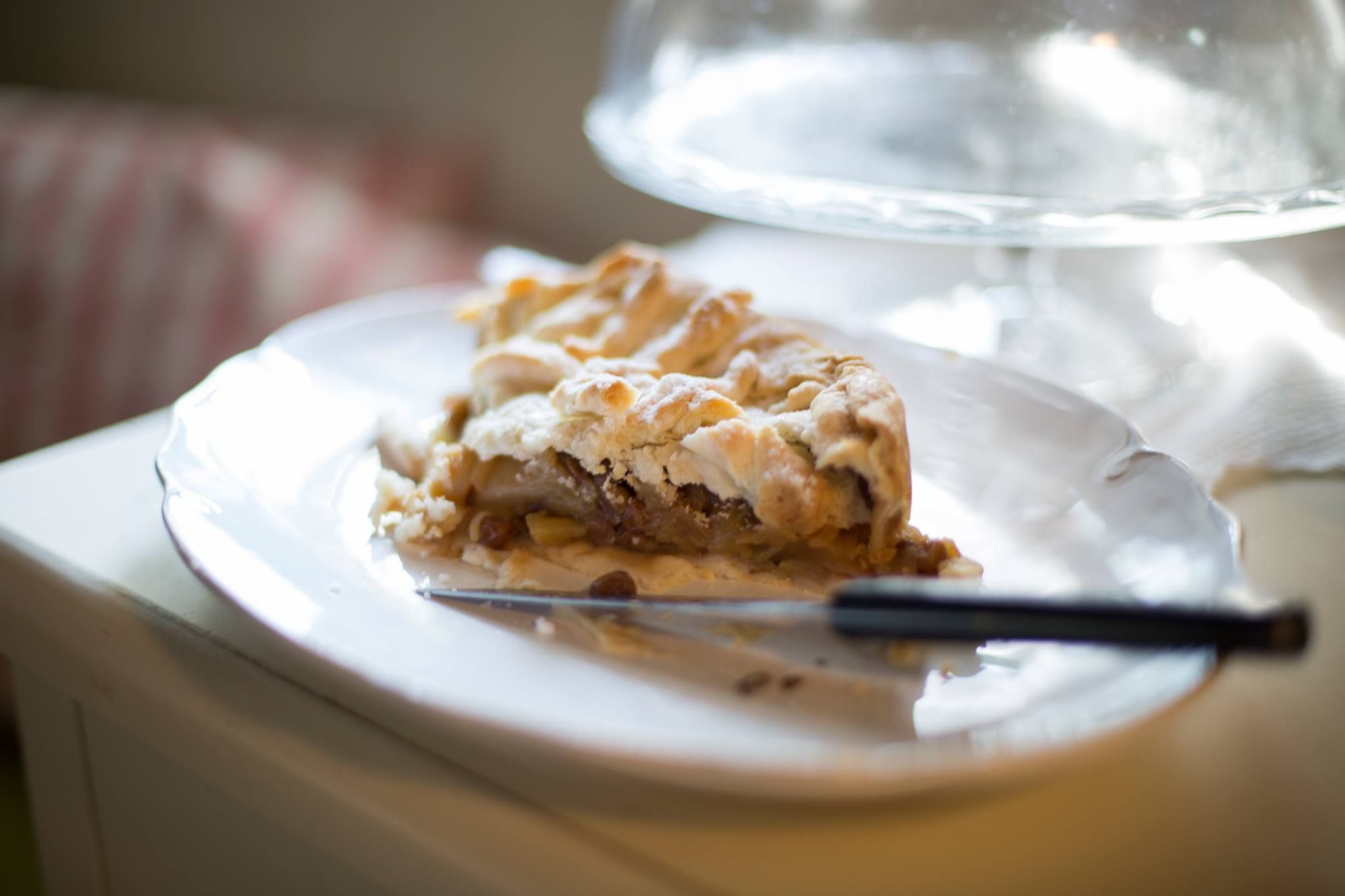 A piece of apple pie on a white plate with a knife next to it.