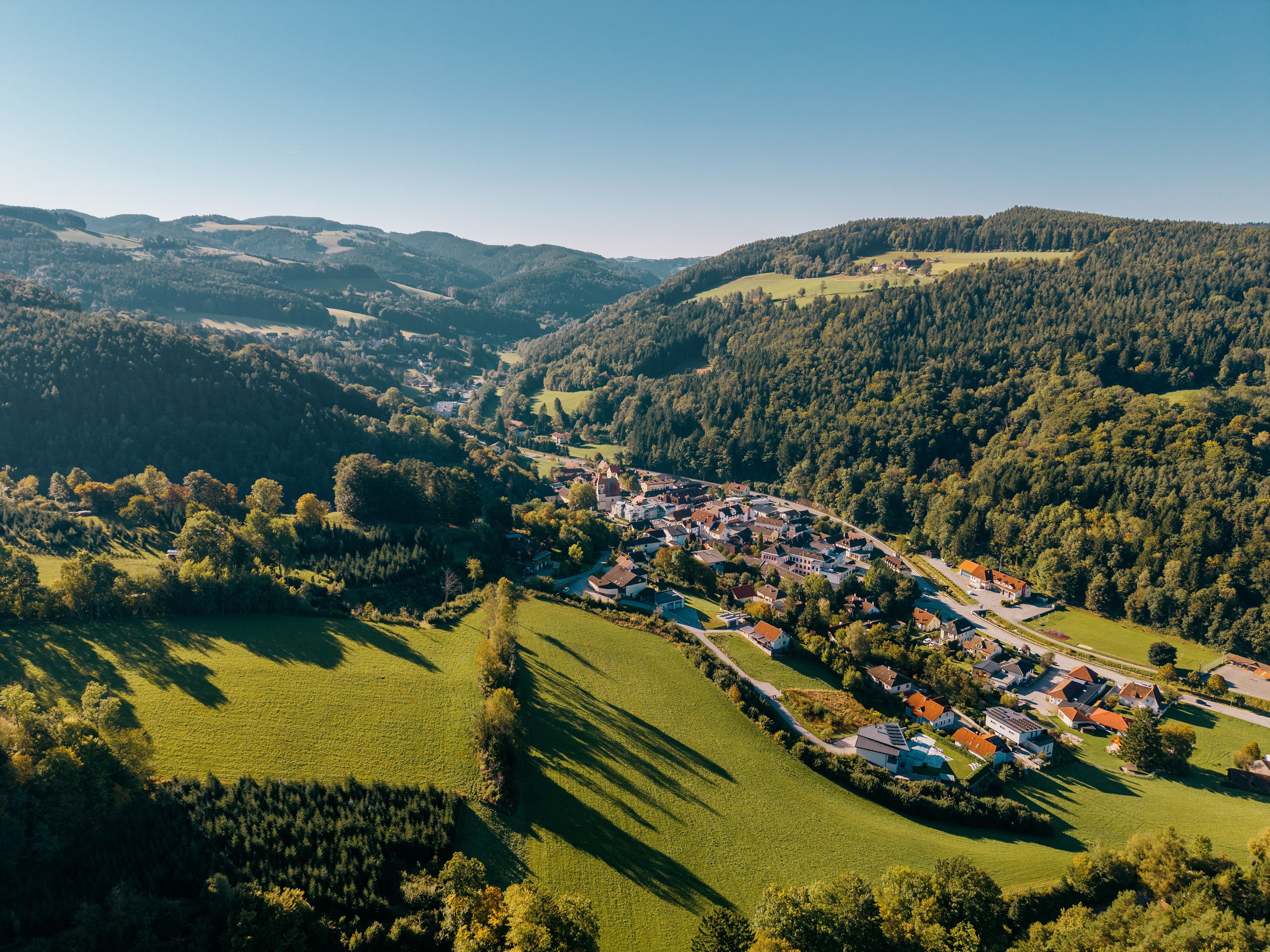 Aerial view of Edlitz with fortified church and surrounding hilly and wooded landscape.