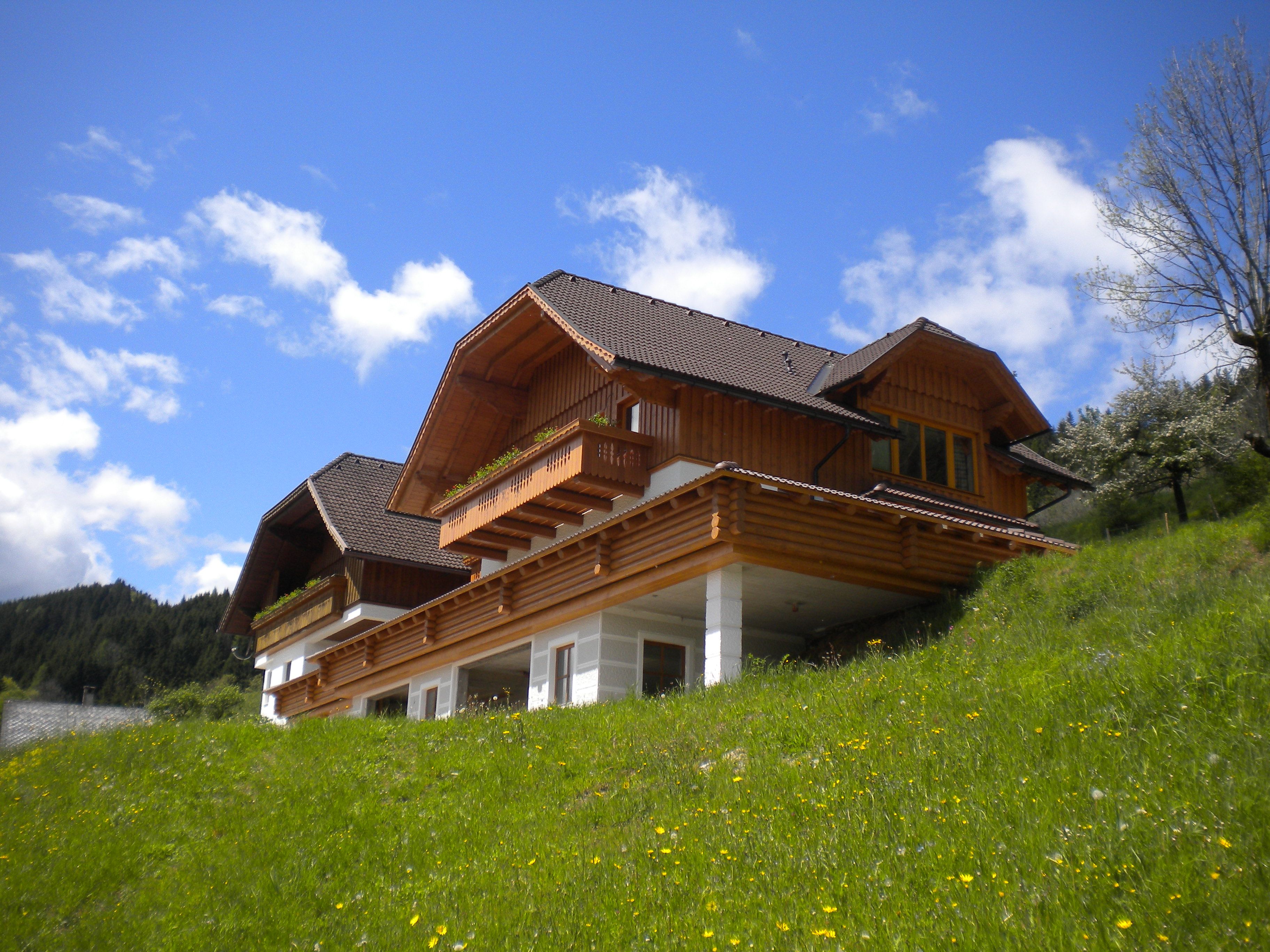 A traditional wooden house on a green hill under a blue sky.